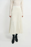 Front detail of an ecru wool-blend midi skirt on a model, showing the wide waistband and accordion pleats, paired with a tucked cream top and black boots.