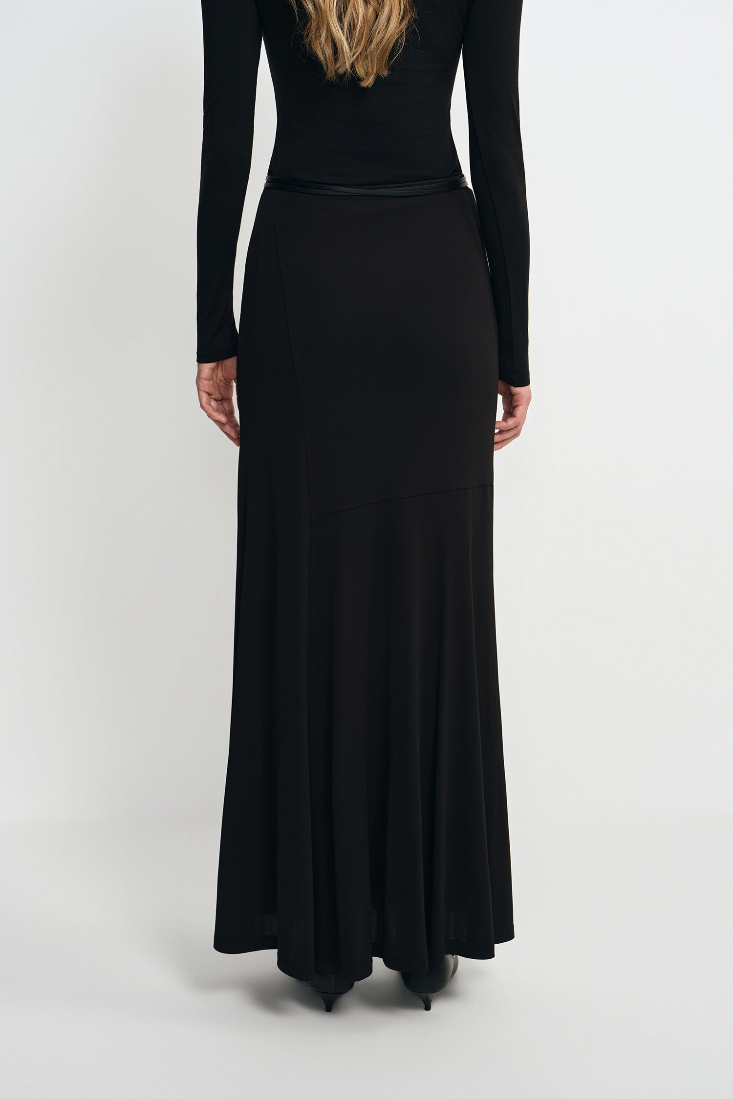 A model wearing a black fluid viscose maxi skirt, back view, showing the A-line sweep.