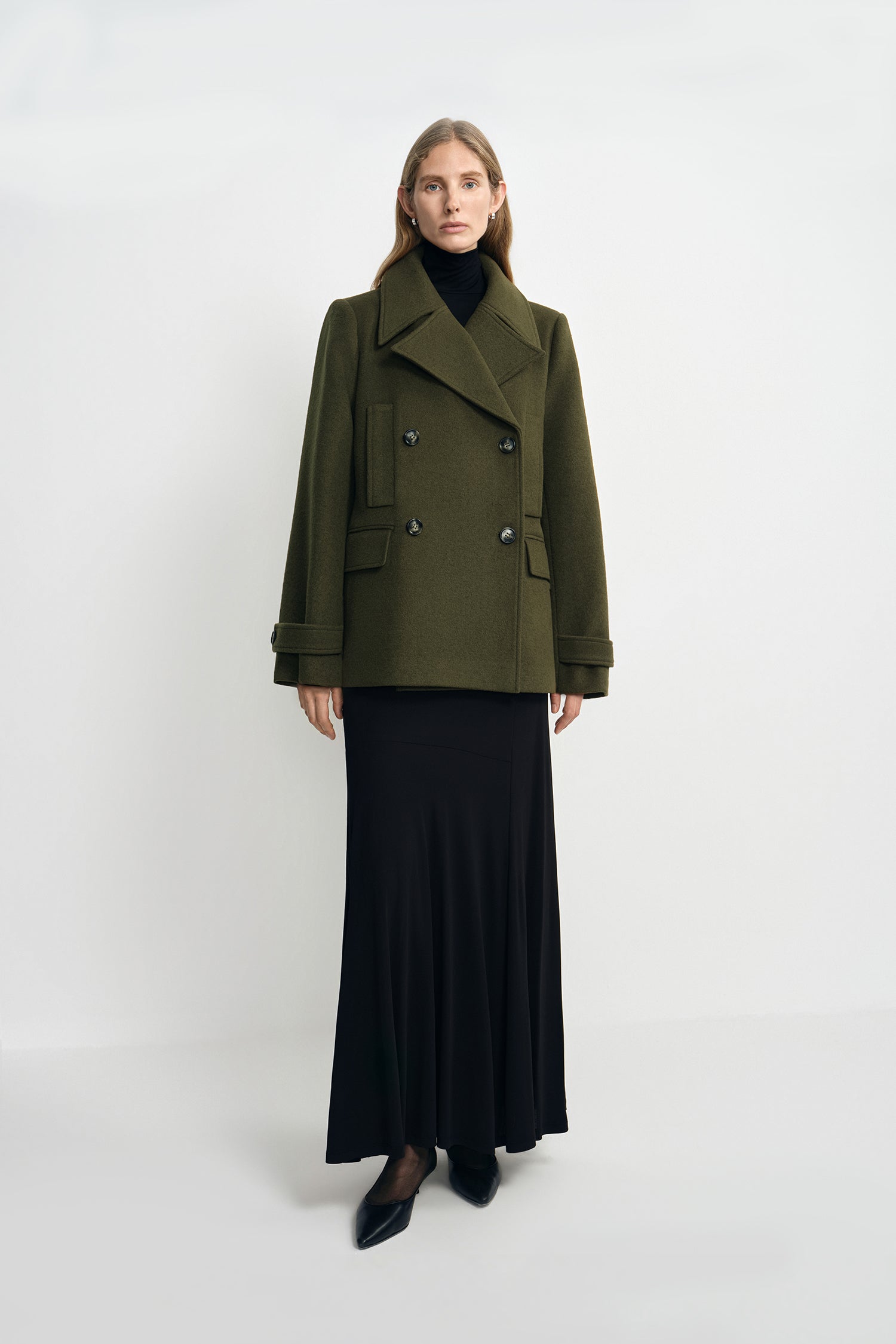A model wearing a black fluid viscose maxi skirt, pairing an olive double-breasted jacket.