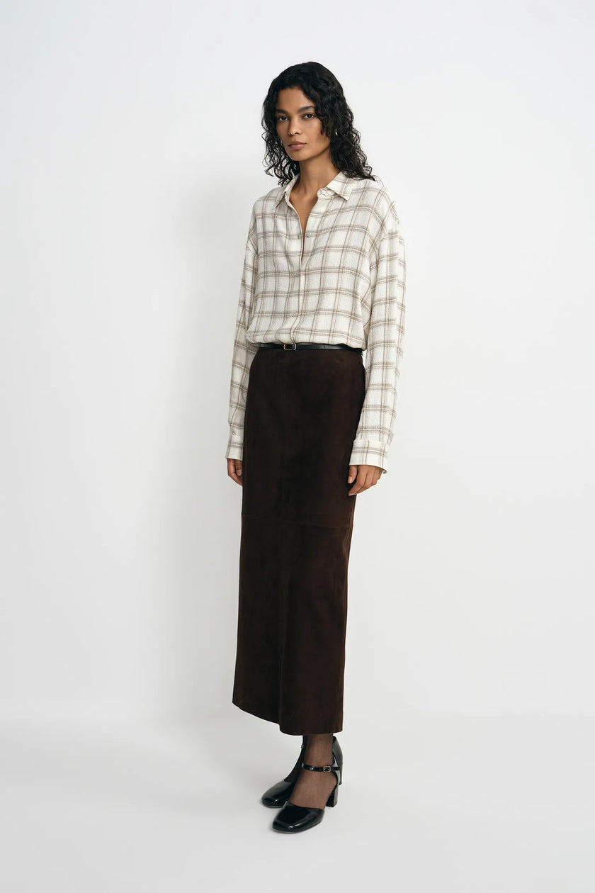 A model stands against a light gray studio background wearing a cream and beige plaid button-up shirt, a dark brown wide-leg skirt, and black Mary Jane heels.