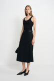Three-quarter view of a model wearing a black wool-blend midi skirt with an overlapping panel, styled with a black tank, slim belt and pointed shoes.