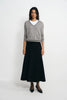 A model stands against a light gray studio background wearing a gray V-neck knit sweater over a white crew-neck undershirt, paired with a long black skirt and black pointed flats.