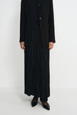 Close-up of a black crinkled maxi skirt showing the elastic waistband, paired with a collarless button-front jacket.