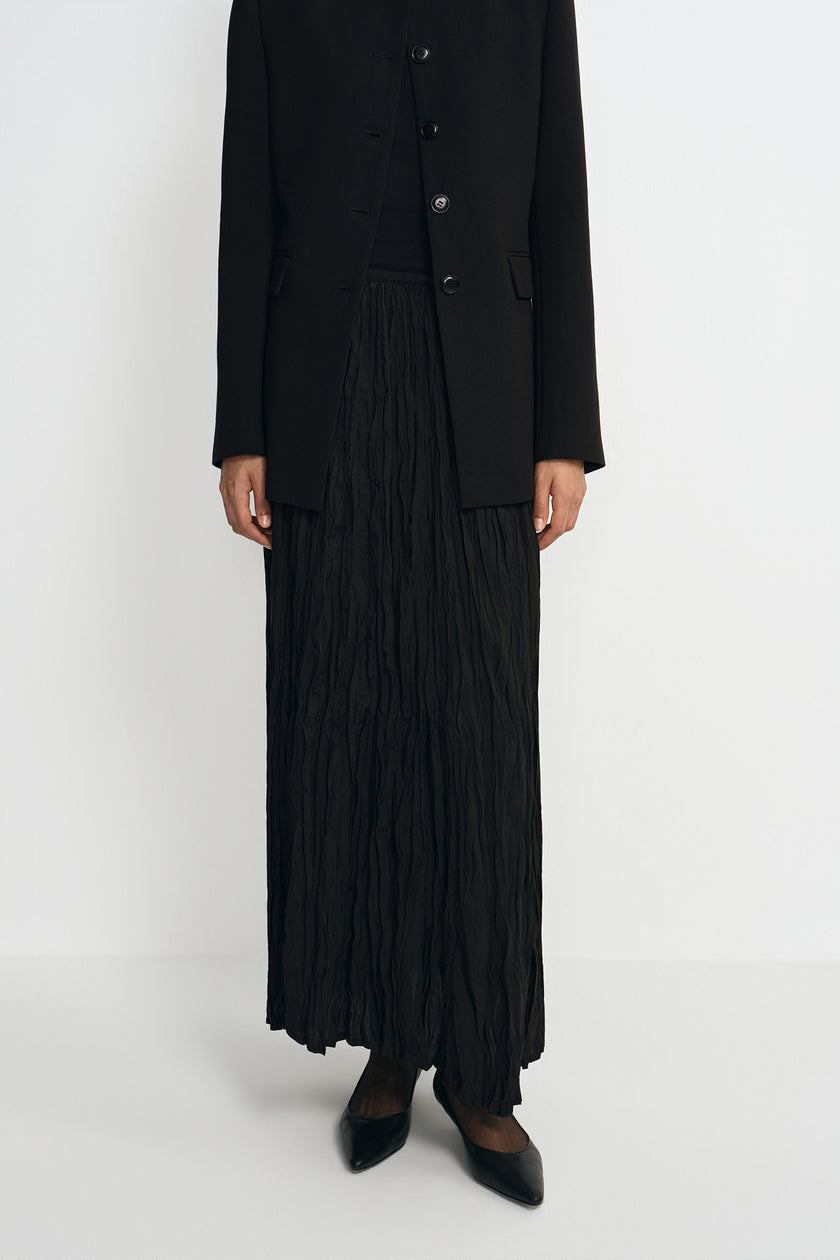 Close-up of a black crinkled maxi skirt showing the elastic waistband, paired with a collarless button-front jacket.