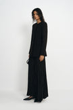 A model wearing a black crinkled maxi skirt, pairing a collarless button-front jacket, side view.