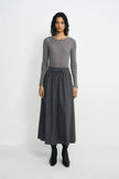 A model stands against a light gray studio background wearing a gray long-sleeve knit top and a matching gray midi skirt with a drawstring waist, paired with black ankle boots.
