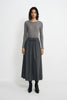 A model stands against a light gray studio background wearing a gray long-sleeve knit top and a matching gray midi skirt with a drawstring waist, paired with black ankle boots.