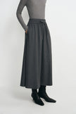 A model wearing a dark gray wide-leg midi skirt with an elastic waistband and drawstring, styled with a gray long-sleeve top and black ankle boots against a light gray studio background.