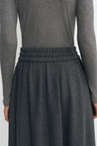 Close-up of a person wearing a dark gray ribbed knit long-sleeve top and a matching dark gray pleated skirt with an elastic waistband.