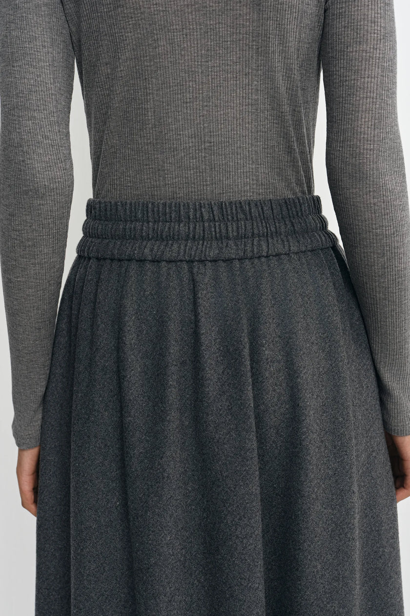 Close-up of a person wearing a dark gray ribbed knit long-sleeve top and a matching dark gray pleated skirt with an elastic waistband.