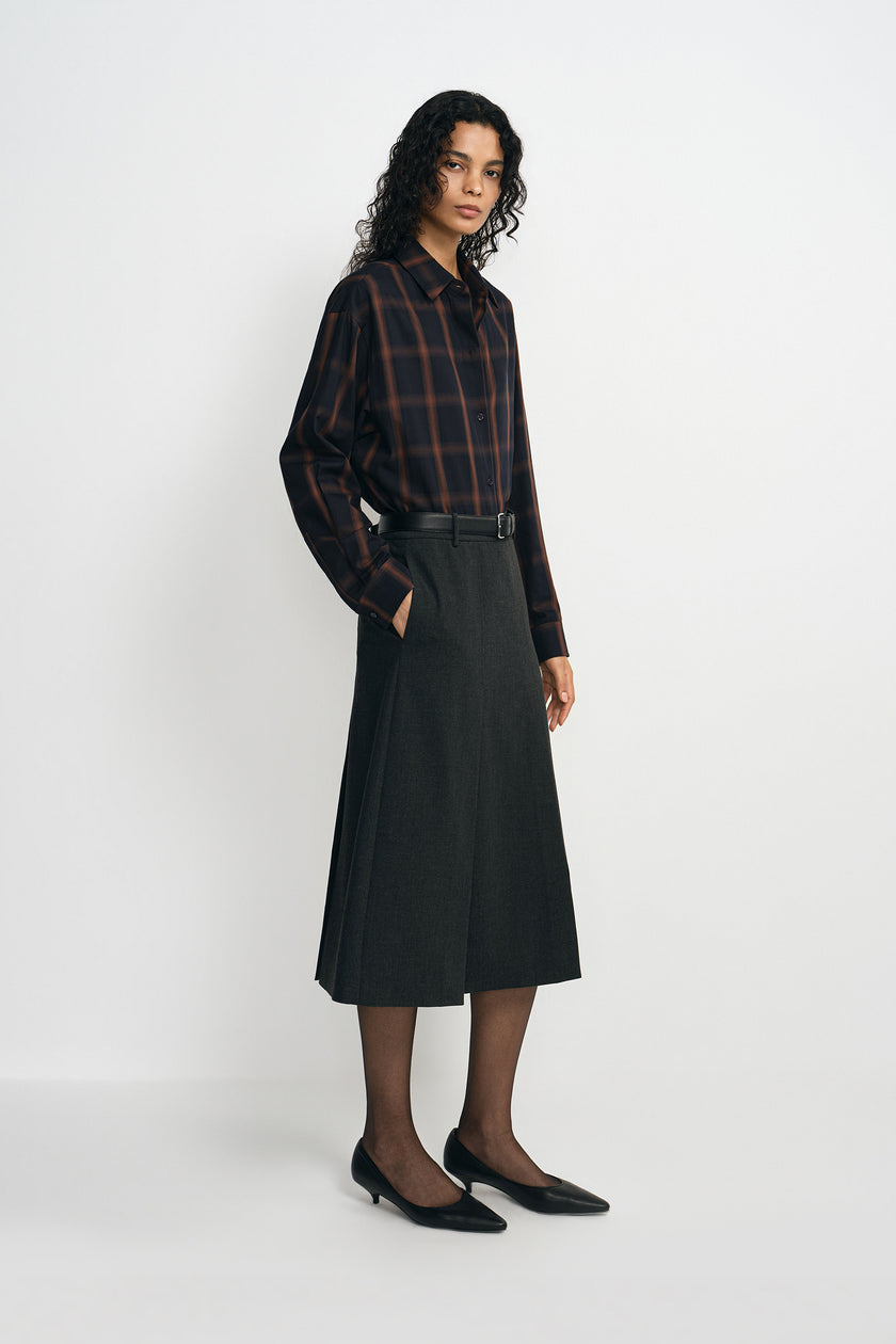 A model wearing a charcoal A-line skirt with a belted waist and side pocket, pairing a plaid button-up shirt, side view.