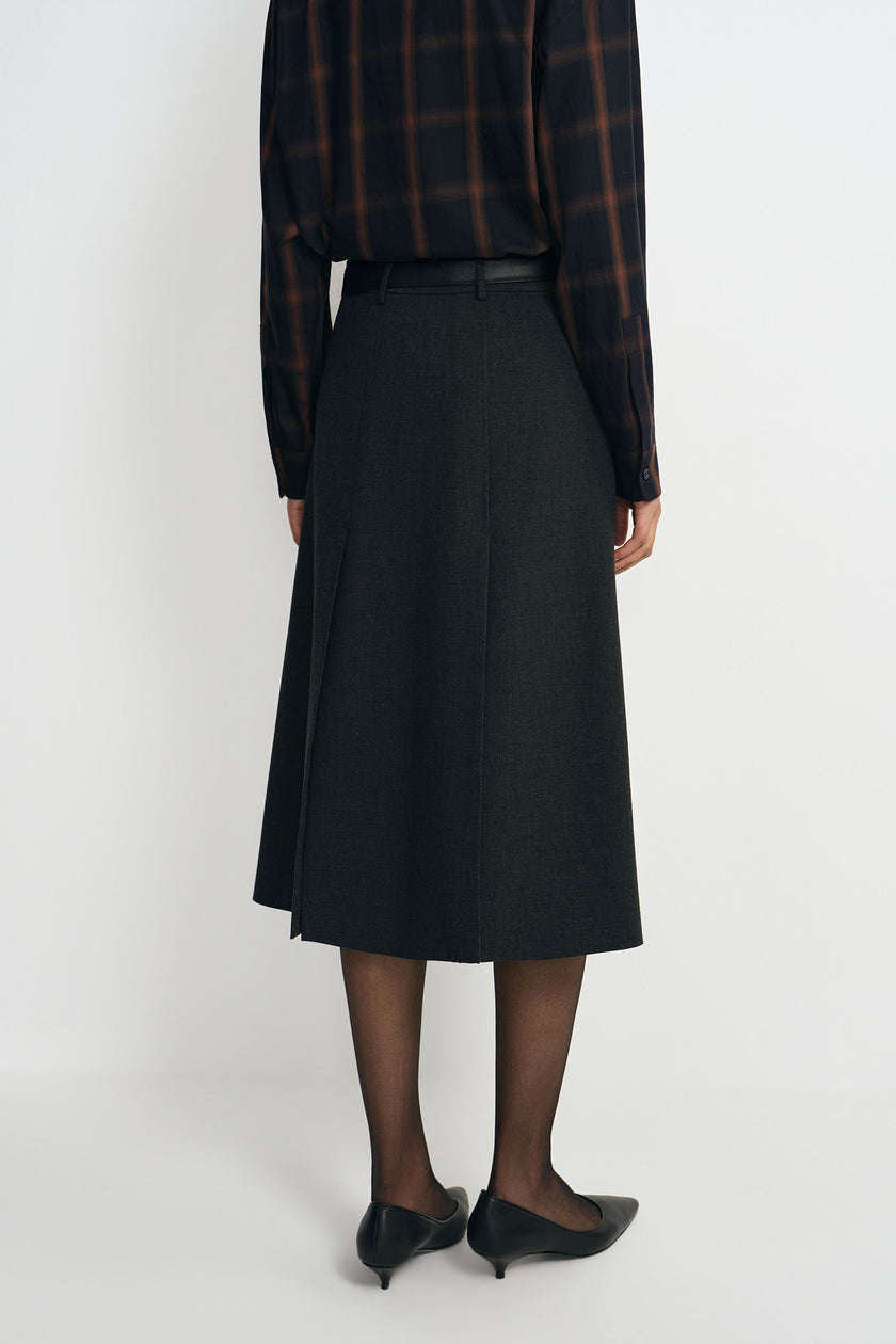 A model wearing a charcoal A-line skirt with a vented back pleat, pairing a plaid button-up shirt, back view.