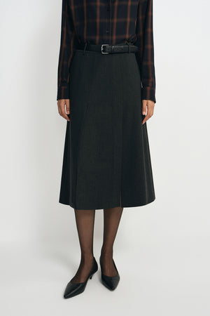 A model wearing a charcoal A-line skirt with a vented front, pairing a plaid button-up shirt.