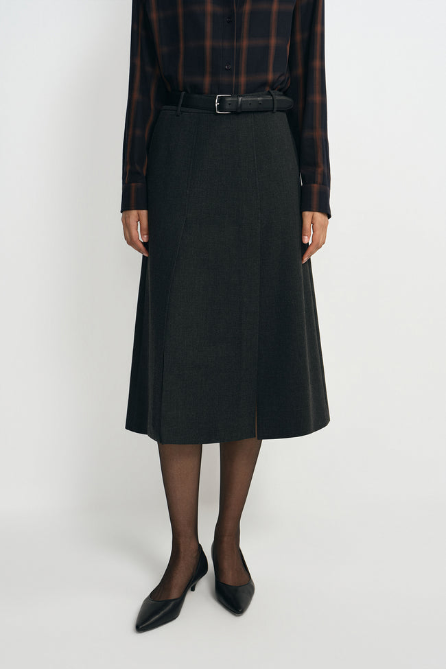 A model wearing a charcoal A-line skirt with a vented front, pairing a plaid button-up shirt.