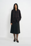 A model wearing a charcoal A-line skirt with a vented front detail, pairing a plaid button-up shirt, facing the camera.
