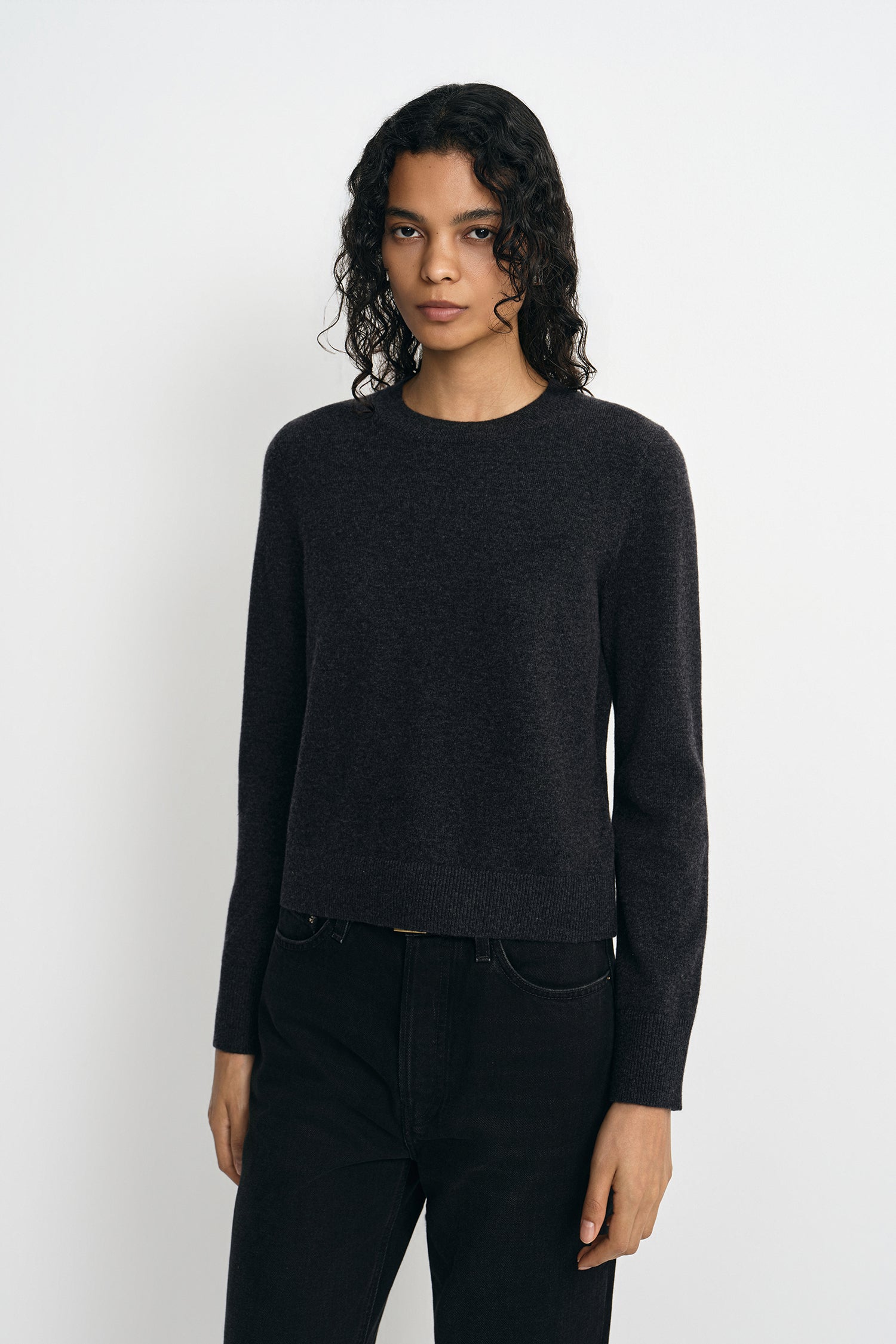 A model wearing a charcoal wool crewneck sweater, facing the camera.