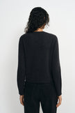 A model wearing a charcoal wool crewneck sweater, pairing black wide-leg jeans, back view.