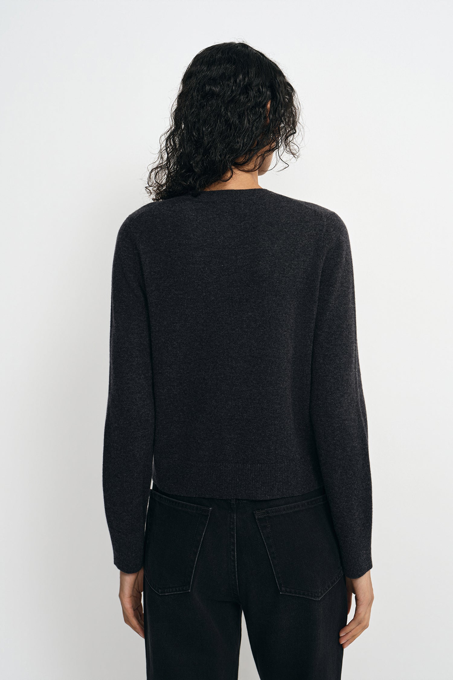 A model wearing a charcoal wool crewneck sweater, pairing black wide-leg jeans, back view.