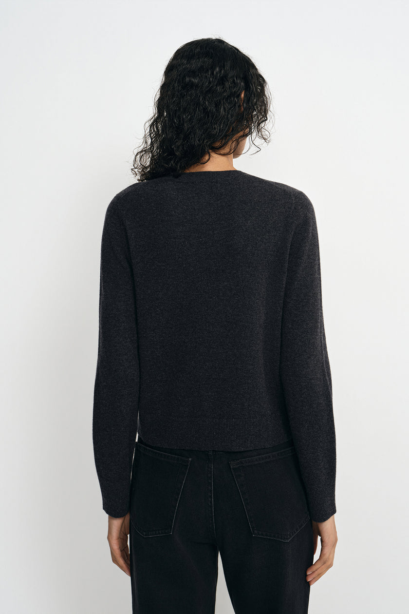 A model wearing a charcoal wool crewneck sweater, pairing black wide-leg jeans, back view.
