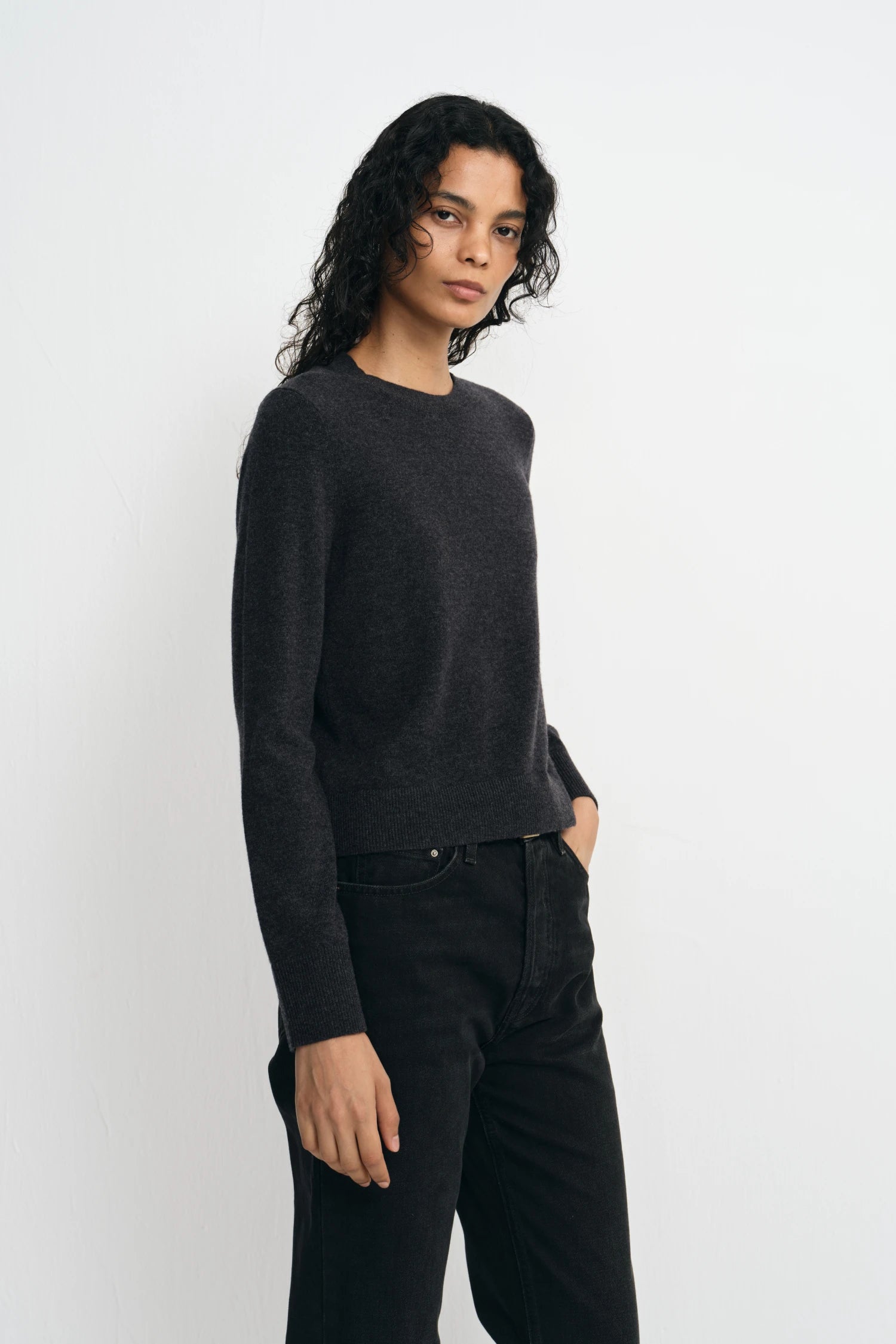 A model wearing a charcoal wool crewneck sweater, pairing black wide-leg jeans, side view.