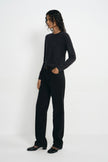 A model wearing a dark charcoal gray long-sleeve knit top and black wide-leg trousers, standing in profile against a clean white studio background.