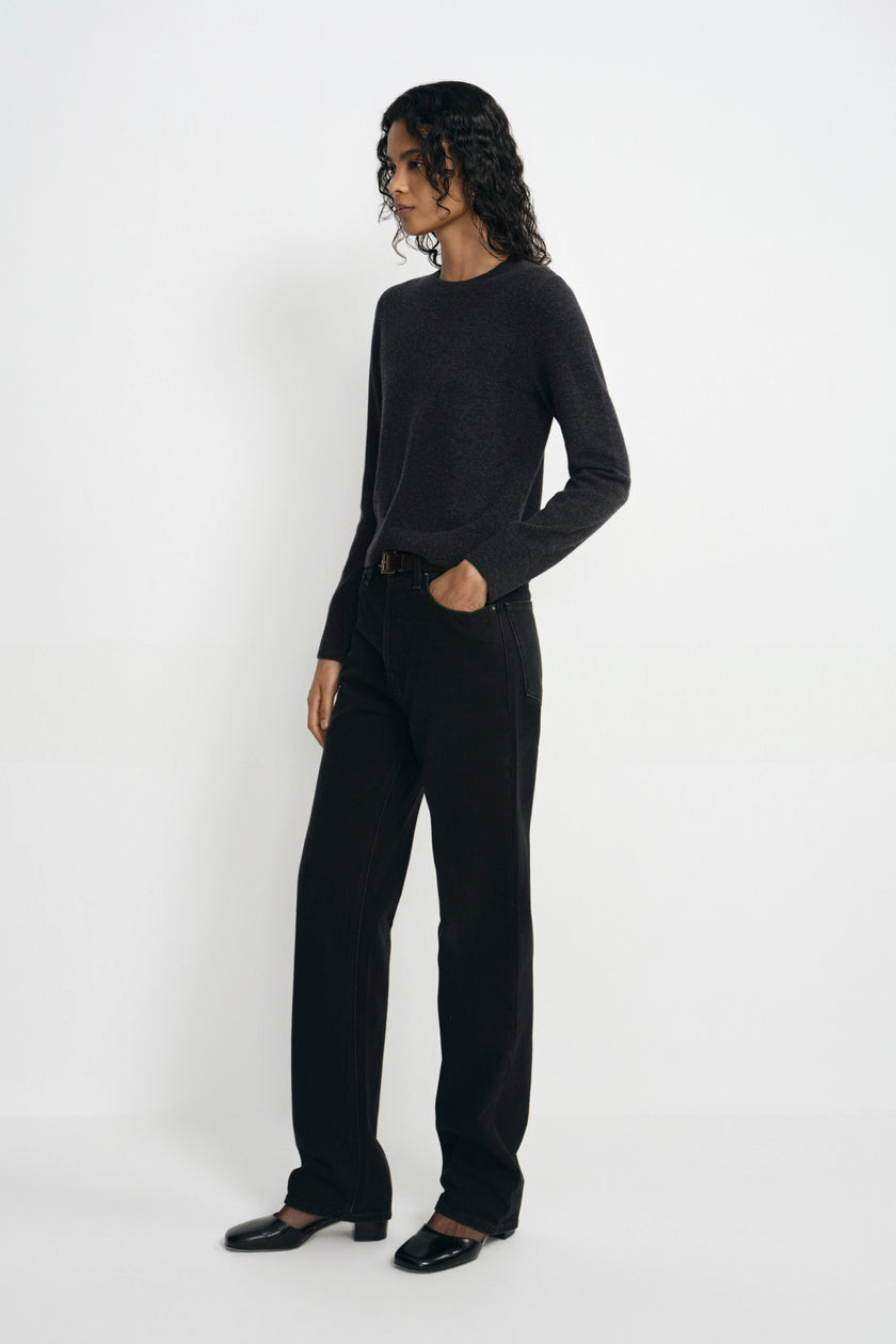 A model wearing a dark charcoal gray long-sleeve knit top and black wide-leg trousers, standing in profile against a clean white studio background.