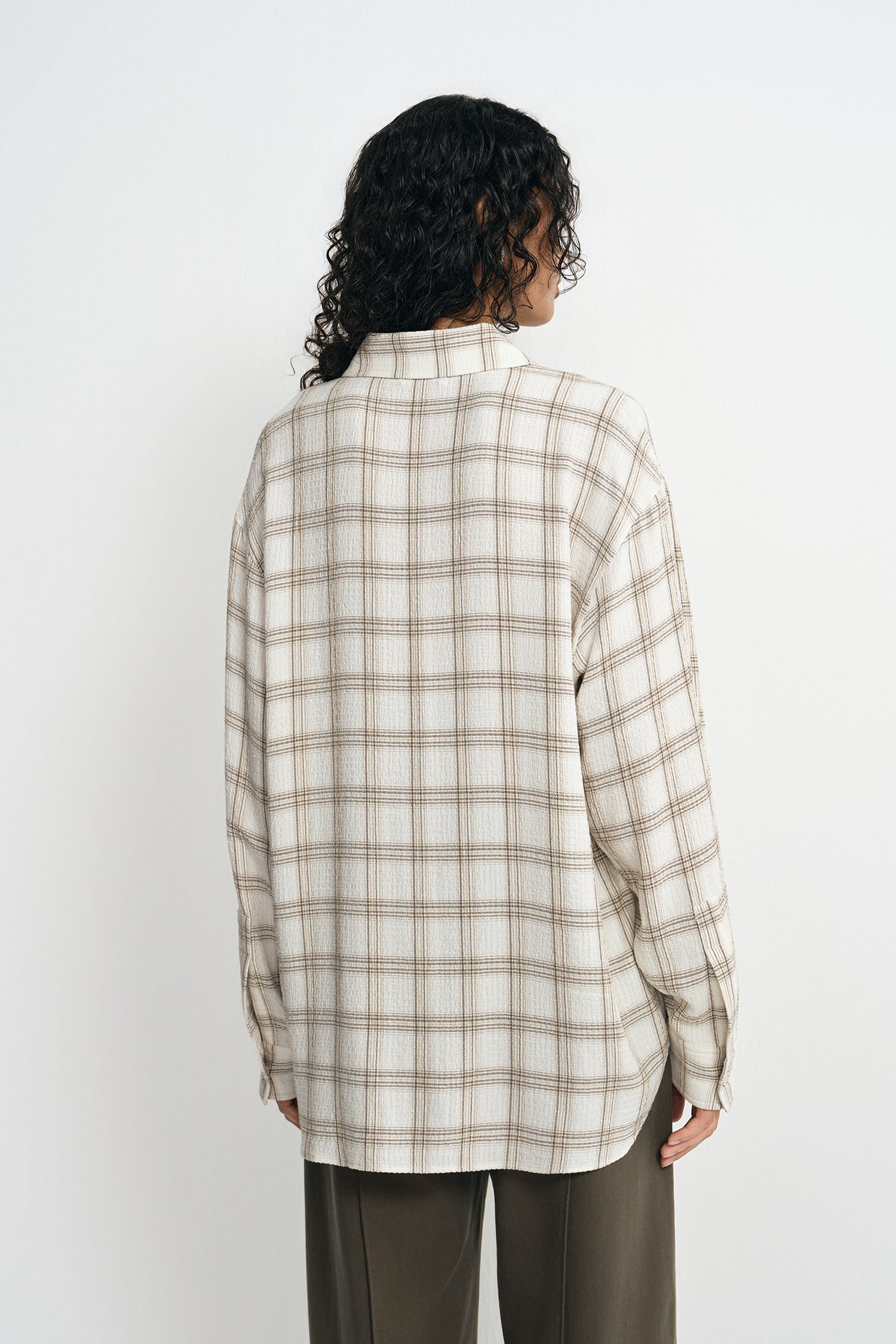 A model wearing a fluid plaid shirt, pairing forest wide-leg trousers, back view.