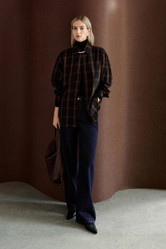 A model wearing Rue Sophie’s Elouet Plaid Oversized Shirt in Navy Plaid, layered over a black turtleneck with dark denim for a relaxed oversized look.