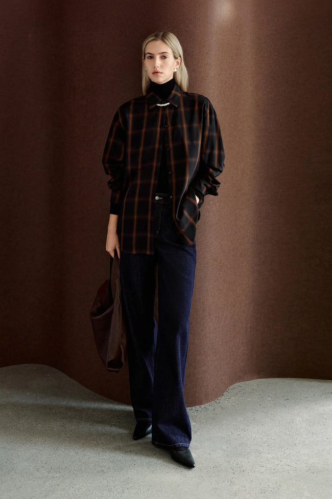 A model wearing Rue Sophie’s Elouet Plaid Oversized Shirt in Navy Plaid, layered over a black turtleneck with dark denim for a relaxed oversized look.