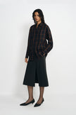 A model wearing a plaid button-up shirt, pairing a charcoal A-line midi skirt, turned slightly to the side.