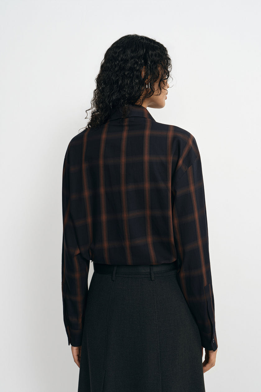 A model wearing a plaid button-up shirt, pairing a charcoal midi skirt, back view.