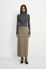 A model stands against a plain white studio background wearing a dark gray ribbed turtleneck sweater and a long taupe skirt, paired with black Mary Jane shoes.