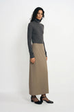 A model stands in a studio wearing a dark gray mock-neck long-sleeve top and a high-waisted, knee-length taupe skirt, paired with black shoes.