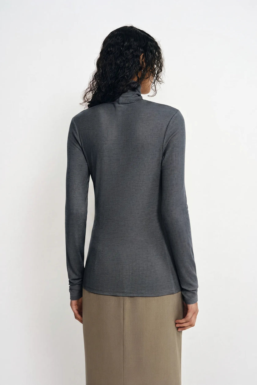 A woman shown from the back wearing a dark gray ribbed long-sleeve mock neck top and a beige skirt, against a plain white background.