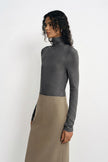 A model wearing a dark gray long-sleeve mock neck top paired with a beige midi skirt, photographed against a plain white studio background.