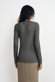 A woman shown from the back wearing a fitted long-sleeve ribbed mock neck top in dark gray, paired with a beige skirt, against a plain white studio background.