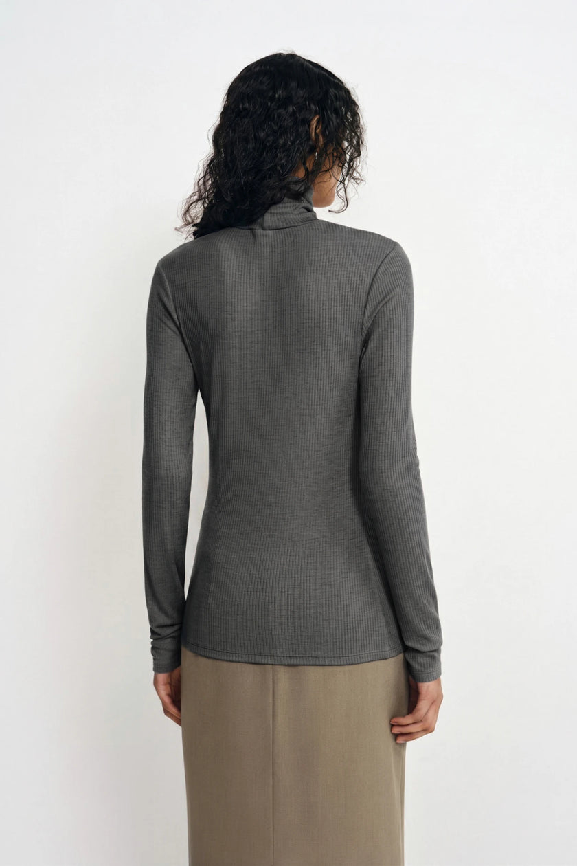 A woman shown from the back wearing a fitted long-sleeve ribbed mock neck top in dark gray, paired with a beige skirt, against a plain white studio background.