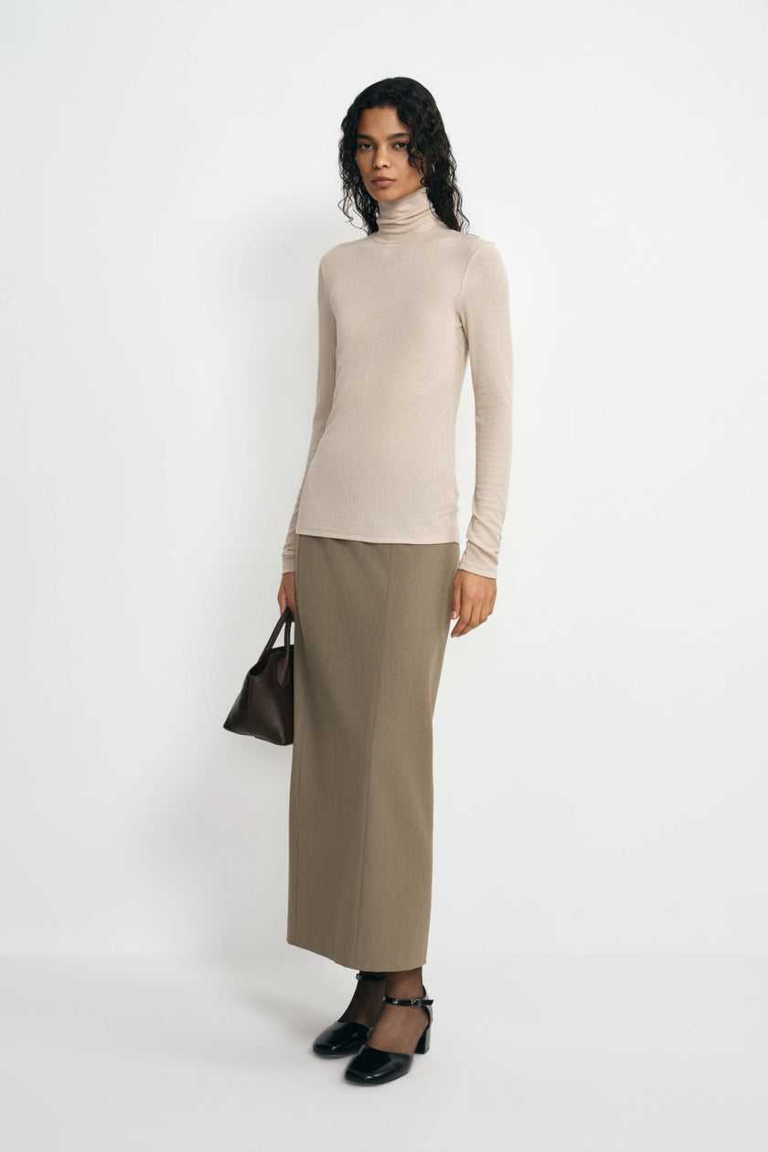 A model wearing a beige ribbed turtleneck top, pairing an oatmeal column skirt, turned slightly to the side.