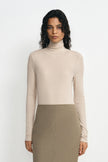 A model wearing a light beige ribbed turtleneck sweater and a taupe pencil skirt, standing against a plain white studio background.
