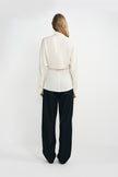 A woman modeling a cream-colored silky wrap-style shirt with long sleeves and classic dark blue jeans.