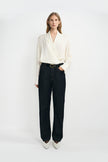 A woman modeling a cream-colored silky wrap-style shirt with long sleeves and classic dark blue jeans, with a classic black cow leather belt, and white pointed kitten heels.