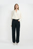 A woman modeling a cream-colored silky wrap-style shirt with long sleeves and classic dark blue jeans, with a classic black cow leather belt, and white pointed kitten heels.