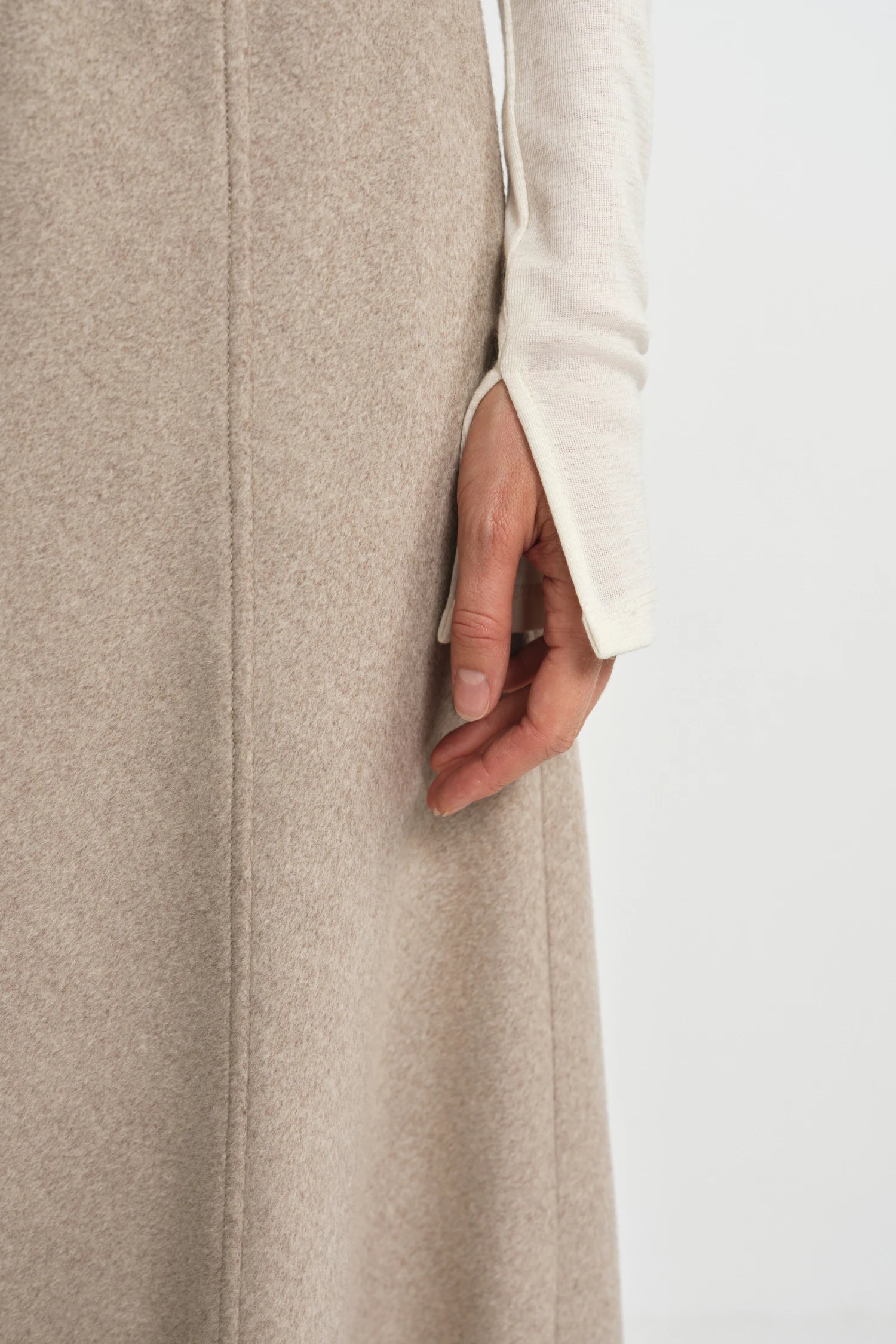Close-up of a khaki flared midi skirt seam detail, paired with an ivory long sleeve top with a slit cuff.