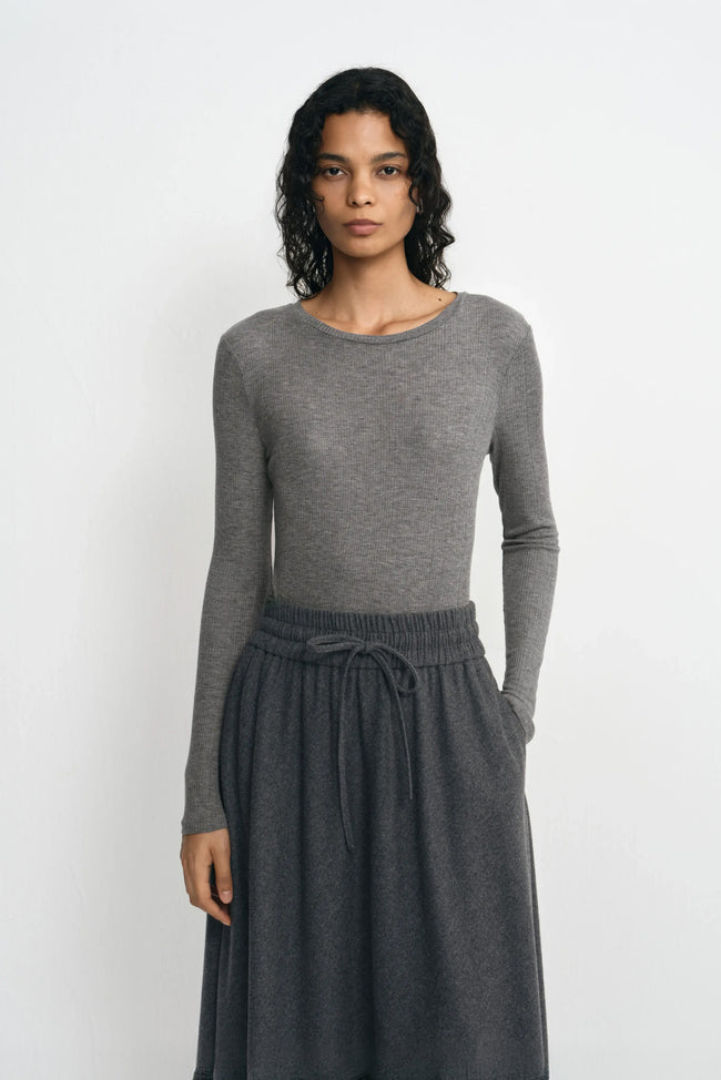 Close-up of a model wearing a medium-grey lyocell-wool top, showing fine ribbing, a narrow crewneck edge and long sleeves above a charcoal skirt.