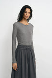 Three-quarter close-up of a model in a medium-grey ribbed top, showing the crew neck and narrow sleeves, with the hem tucked into a charcoal skirt.