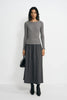 A model wearing a medium-grey ribbed lyocell-wool top with long sleeves and a crew neck, untucked over a charcoal midi skirt with black boots.