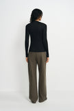 A model wearing a black pleated turtleneck top, pairing olive wide-leg trousers, back view.