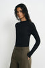 A model wearing a black ribbed long-sleeve mock neck top and olive green trousers, standing against a plain light gray background.