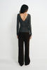 Back view of a model in a charcoal-heather top, showing the deep V-back, long sleeves and gathered waist above dark brown wide-leg trousers.