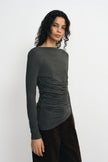 Three-quarter close-up of a charcoal-heather top on a model, showing waist gathers and an angled hem worn over dark brown trousers.